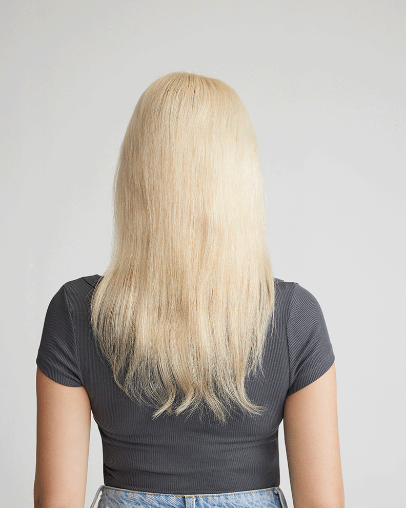 A woman with long blonde hair is seen from the back, showcasing her natural hair before applying hair extensions.