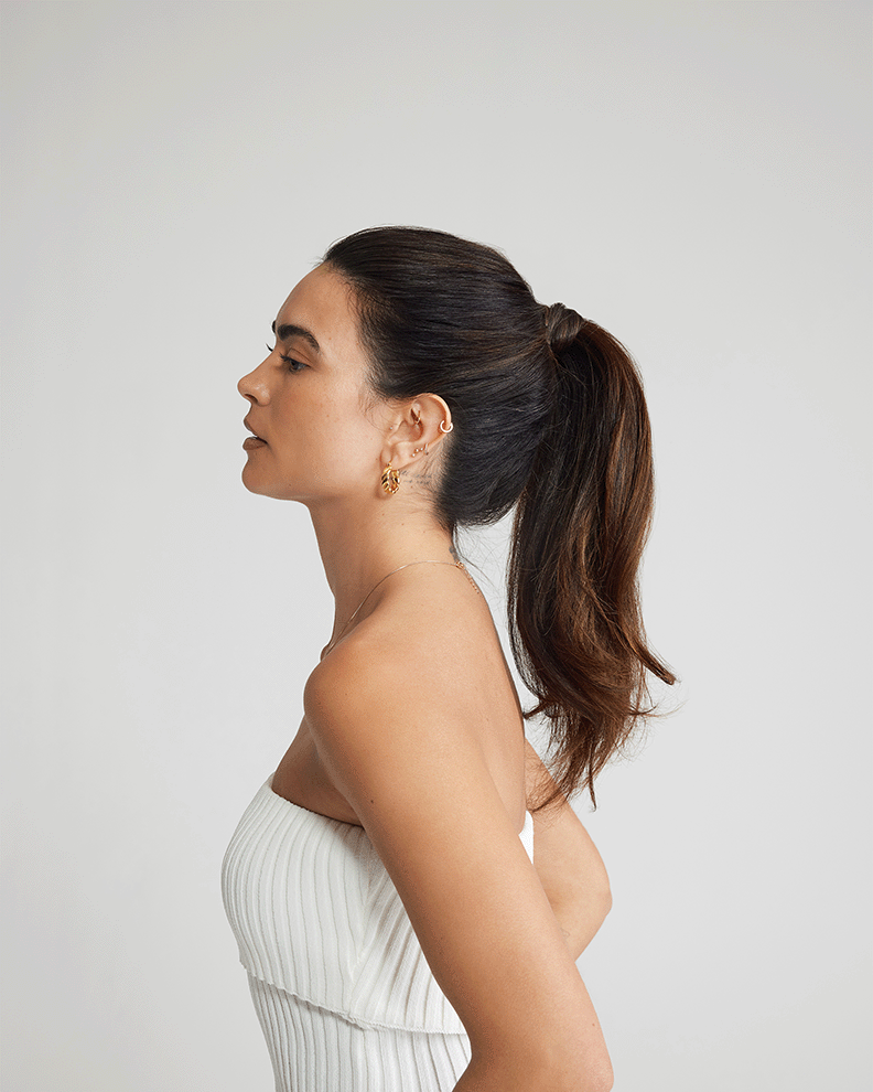 A model in a white dress showcases a sleek ponytail, highlighting her natural hair before applying extensions.