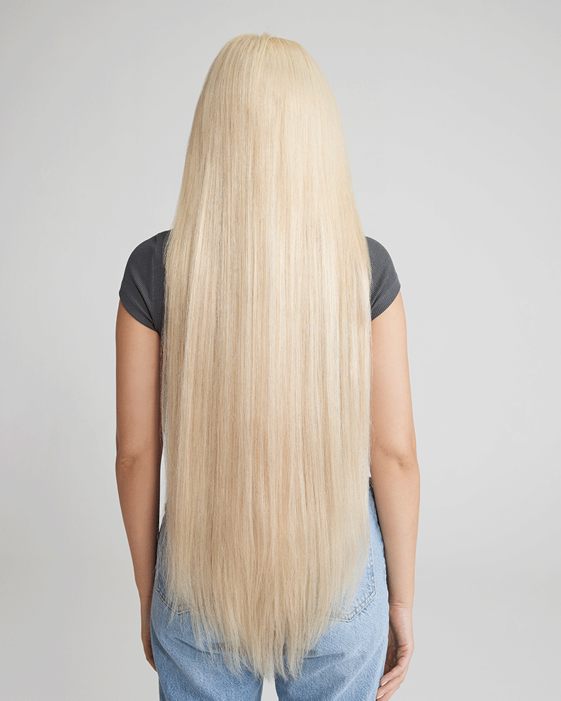 A woman with long blonde hair, viewed from the back, showcasing her hair extensions for added length and volume.