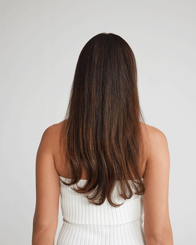A woman's head from the back, showcasing her white dress, highlighting her hair before applying hair extensions.