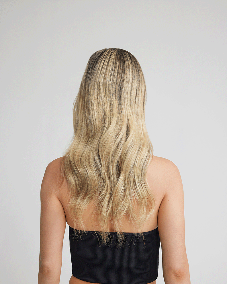 A woman with hair extensions viewed from the back, wearing a stylish black crop top.