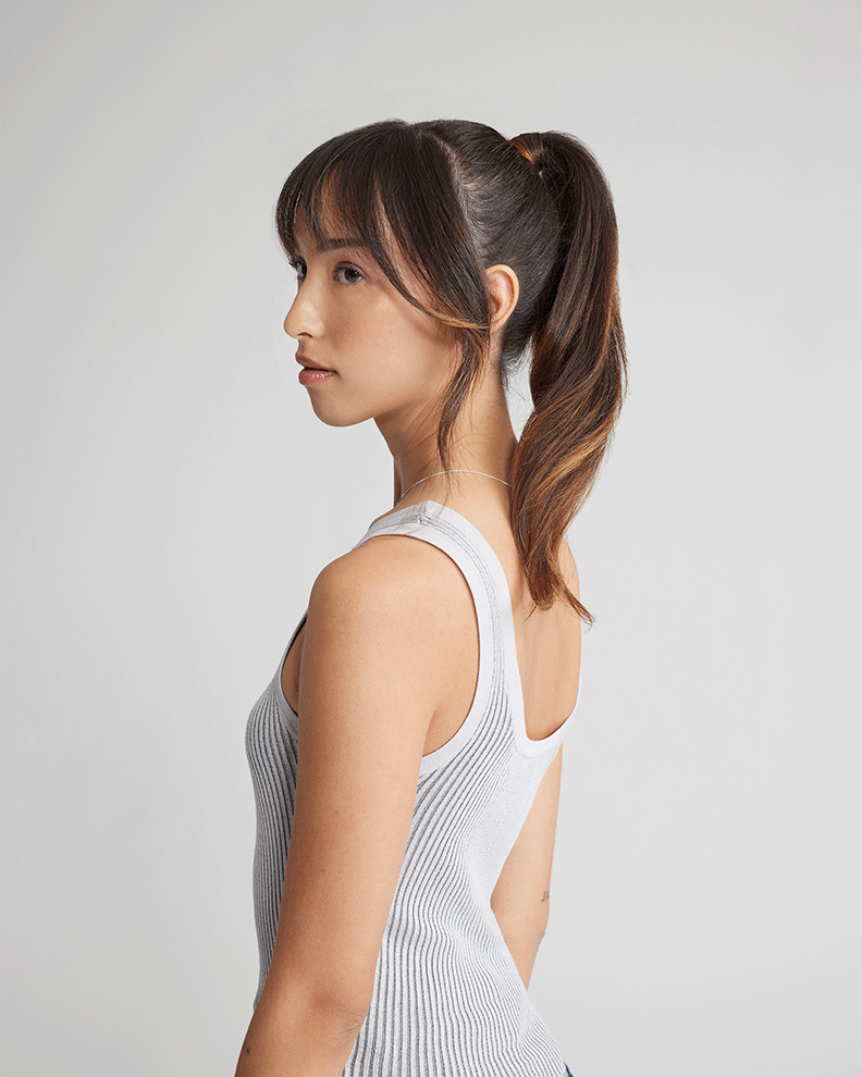 A woman in a grey tank top and ponytail, with her natural hair.
