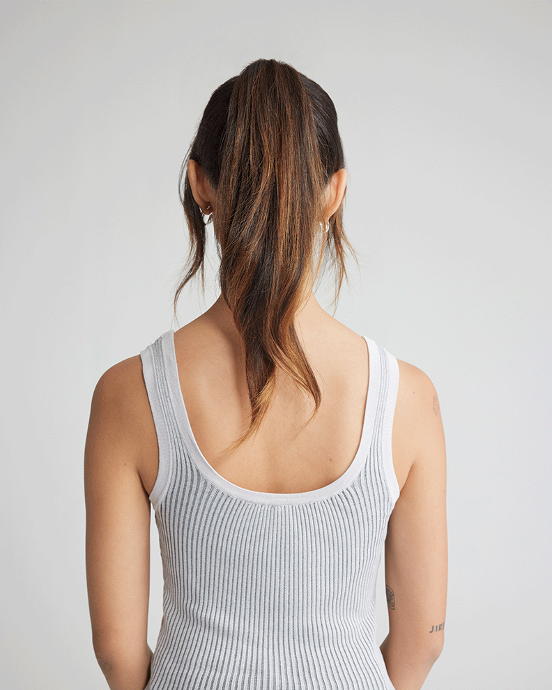 A woman in a grey tank top and ponytail, with her natural hair.