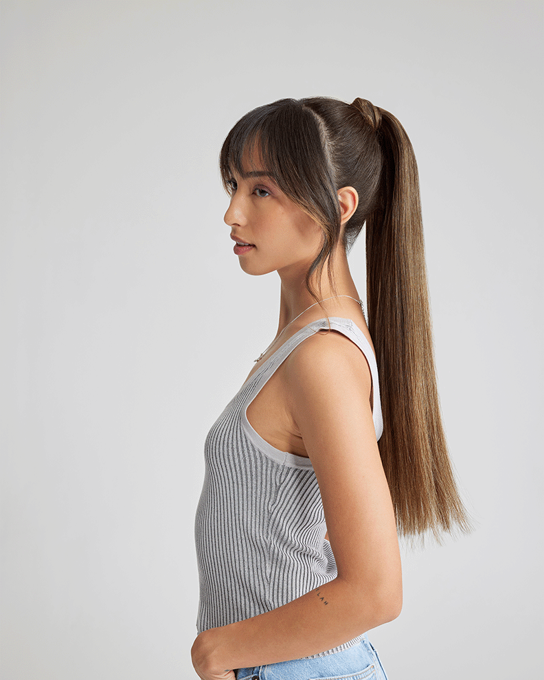 A woman with long hair, enhanced by extensions, wearing a stylish tank top.