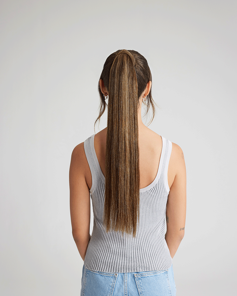 A woman with long, extension-enhanced hair, dressed in a tank top, radiating style and poise.