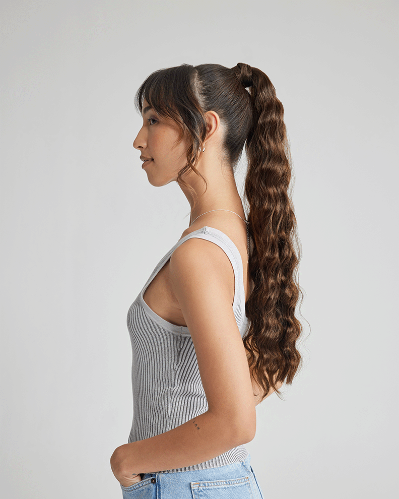 A woman with long, wavy hair styled in a ponytail, showcasing the results of a recent hair extension application.