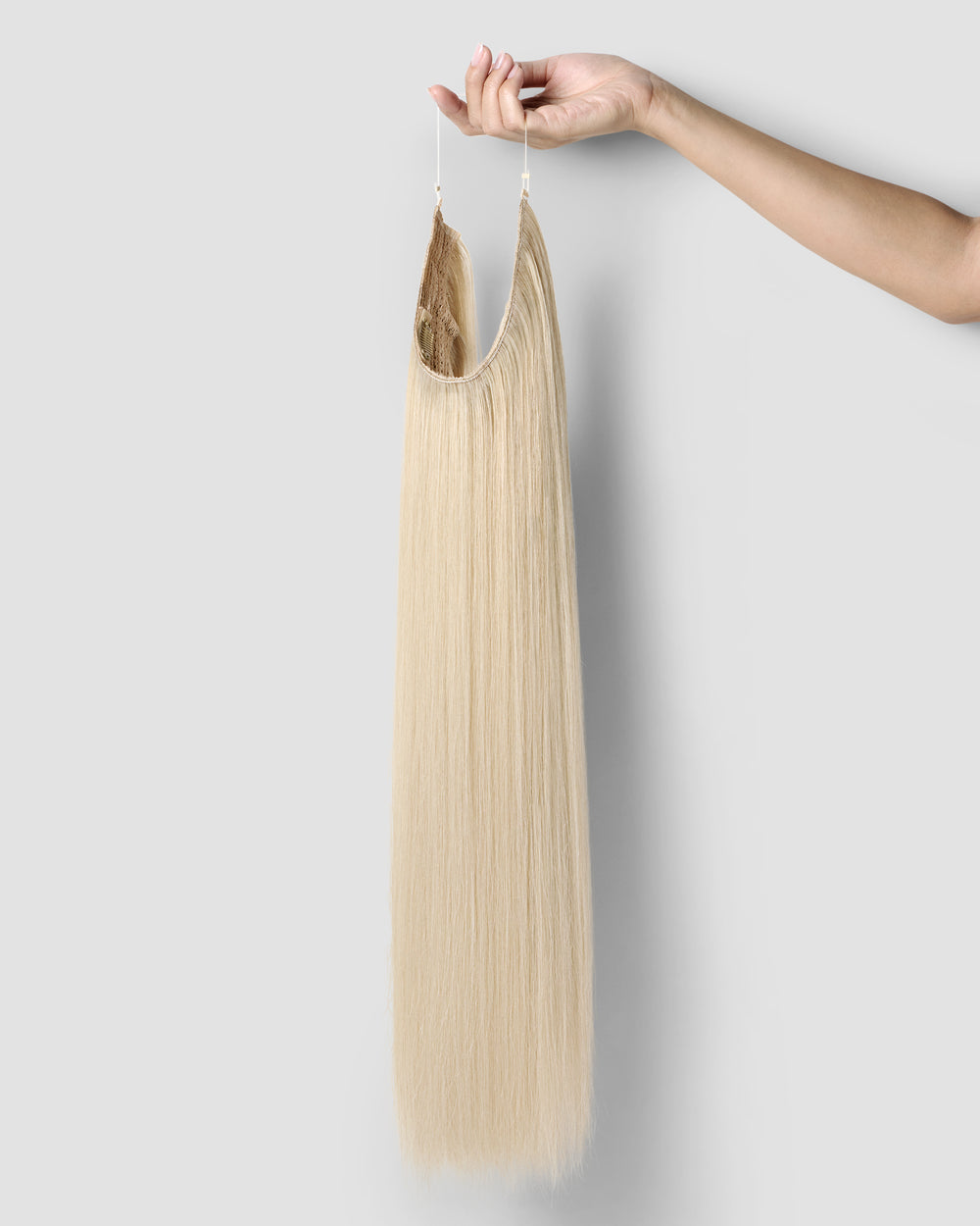 A hand gracefully holds a long, champagne blonde halo extension, showcasing its luxurious texture and color.