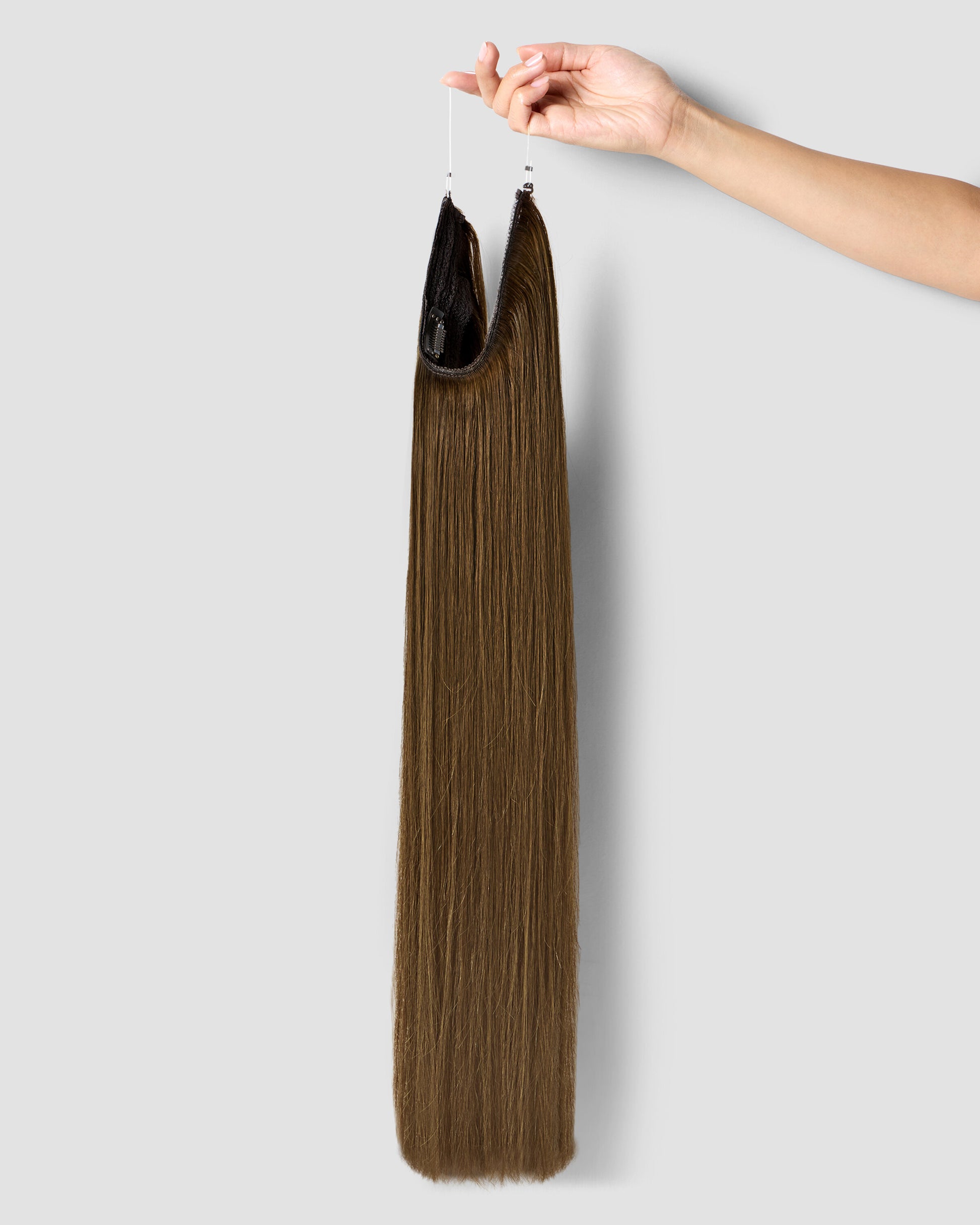 A hand gently holds long chestnut brown hair extensions, showcasing their rich color and texture.
