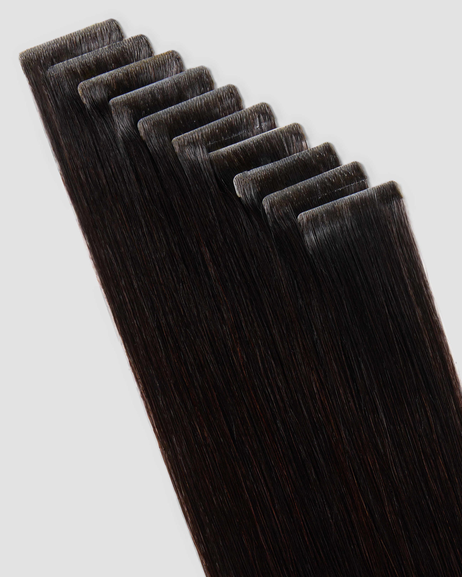 A set of invisi tape in natural black colored hair extensions displayed on a white surface, showcasing their sleek design.