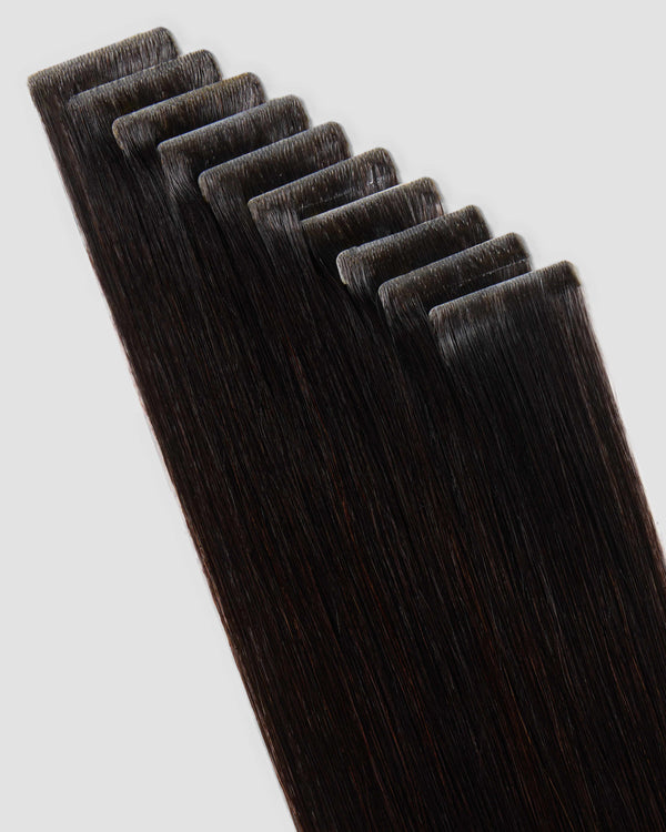 A set of invisi tape in natural black colored hair extensions displayed on a white surface, showcasing their sleek design.
