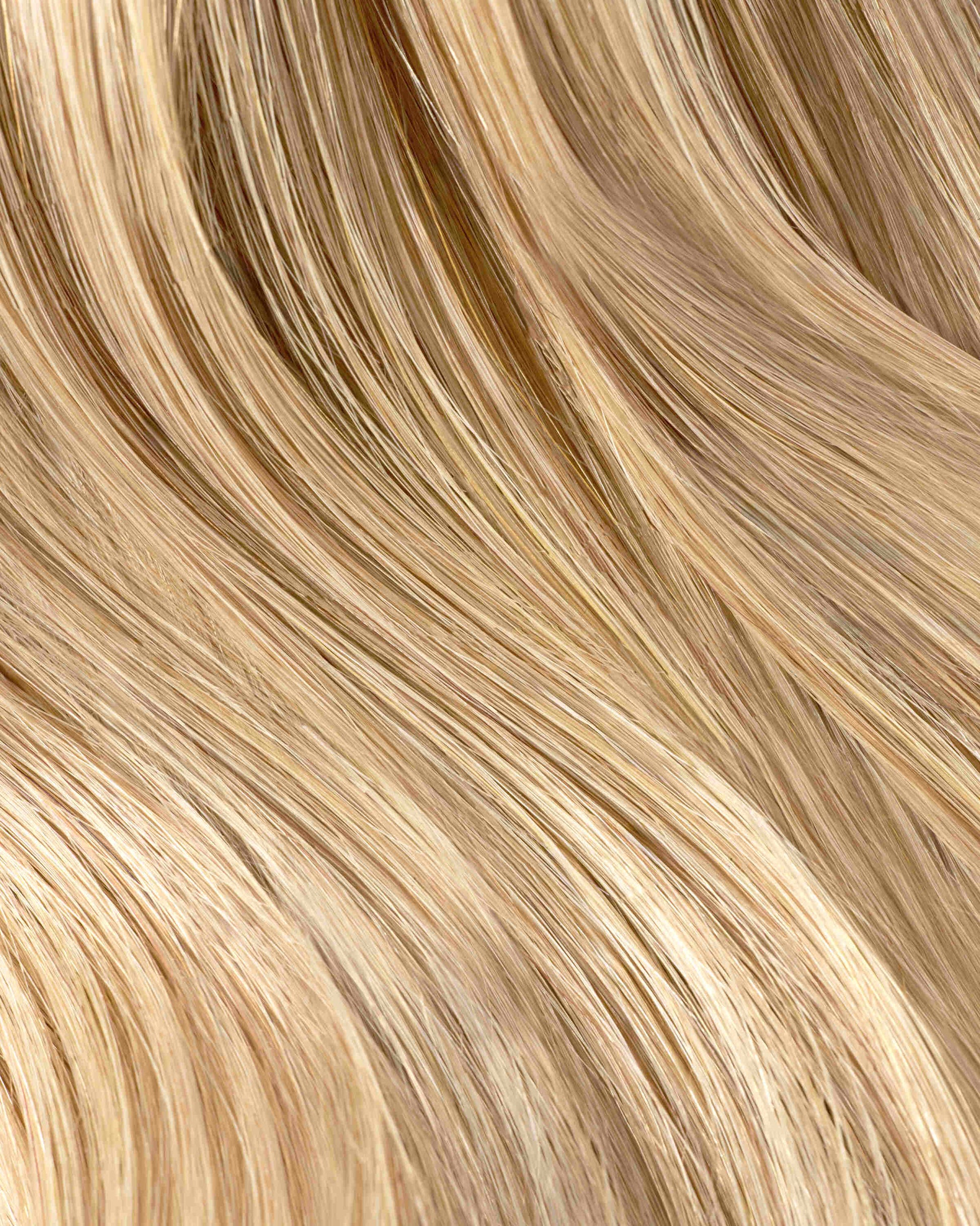 A close-up of wavy honey blonde hair extensions, showcasing soft, light blonde strands with a natural shine.