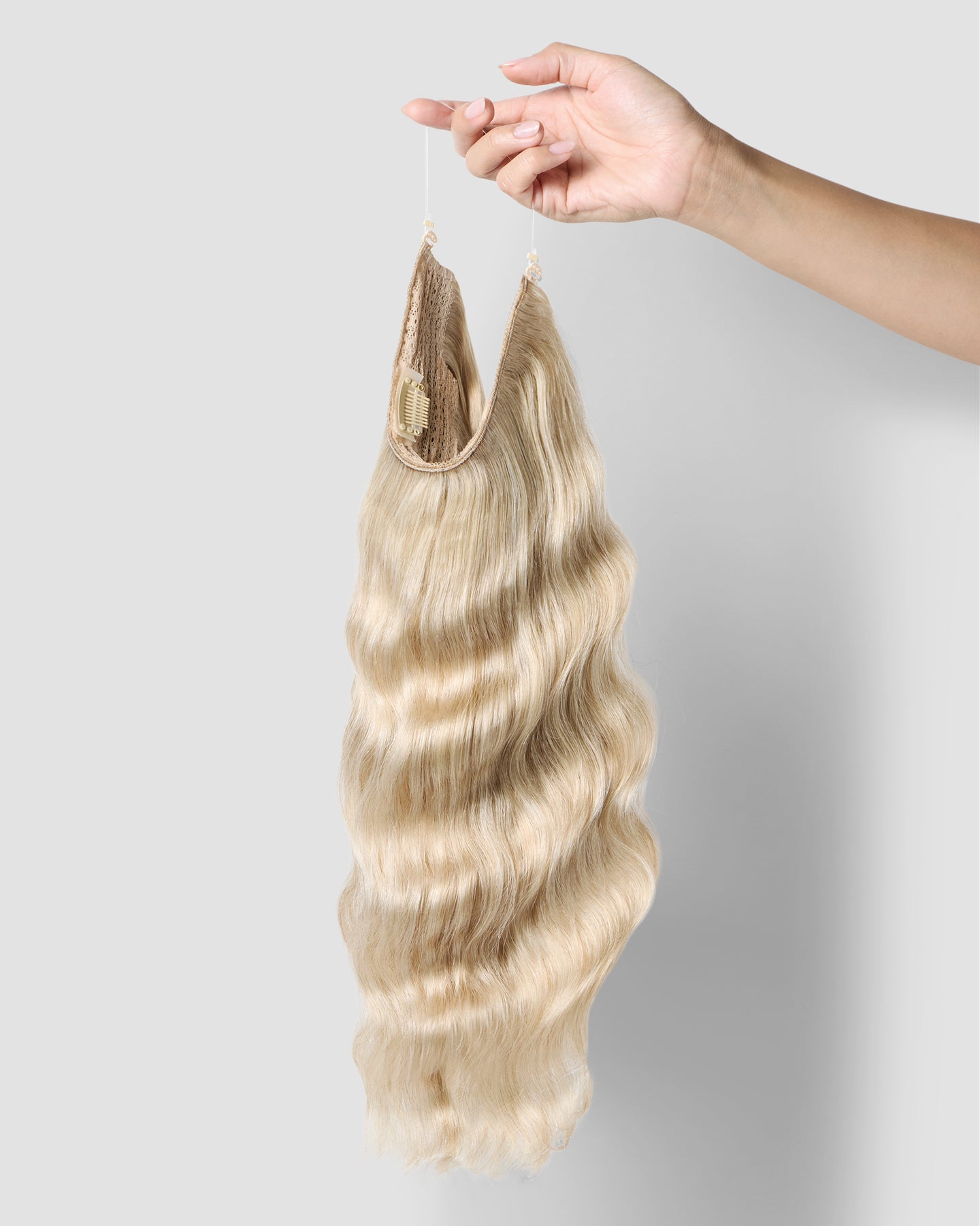 A hand gently holds a long, champagne blonde halo extension, highlighting its smooth texture and vibrant color.