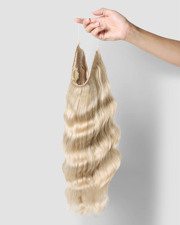 A hand gently holds a long, champagne blonde halo extensions, highlighting its smooth texture and vibrant color.