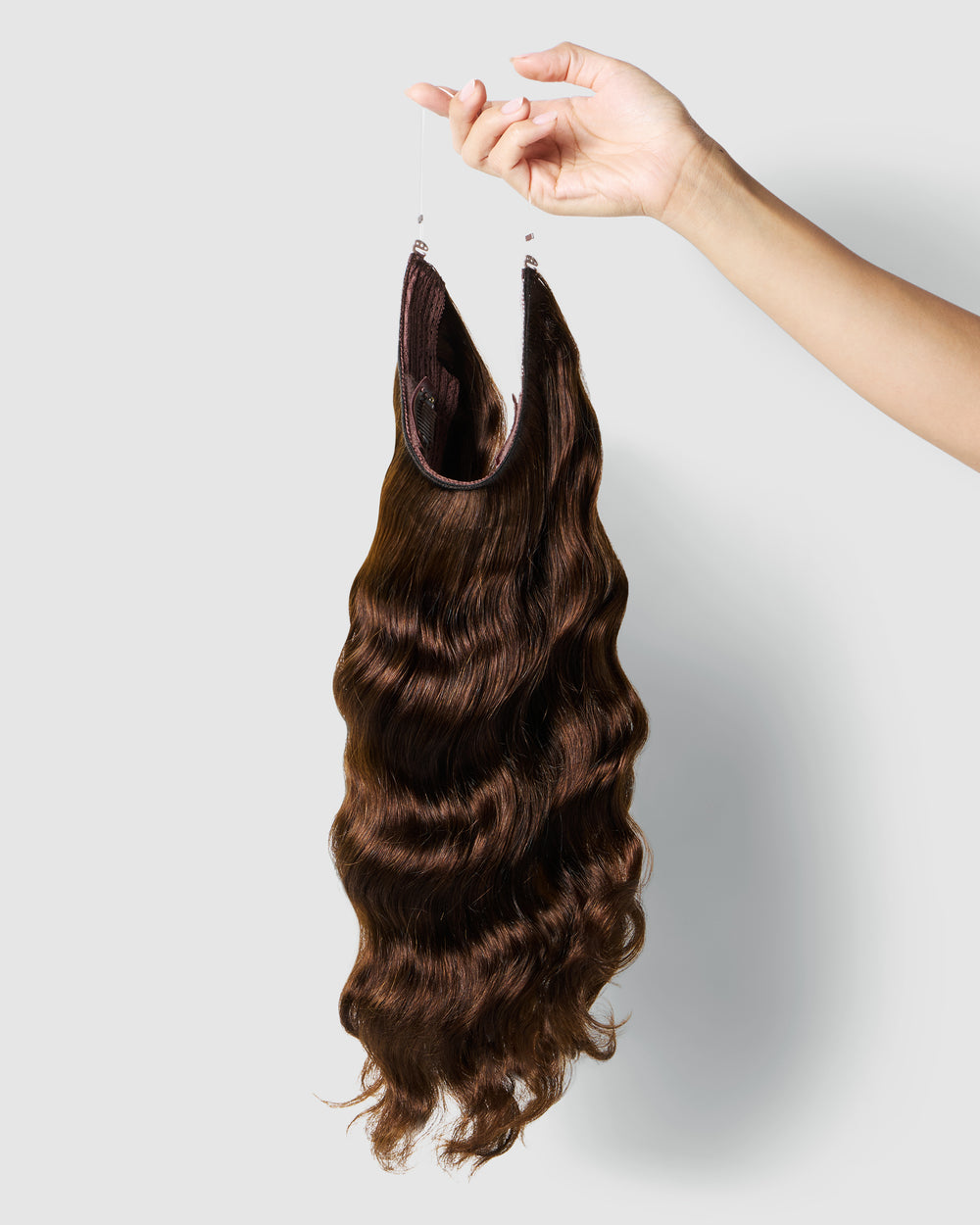 A hand elegantly holds a long, dark chocolate halo extension, highlighting its luxurious texture and deep brown hue.