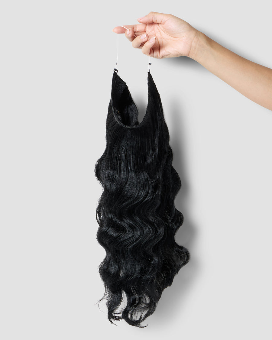 A hand gently holds a long, jet black halo Zala hair extension, showcasing its smooth texture and length.
