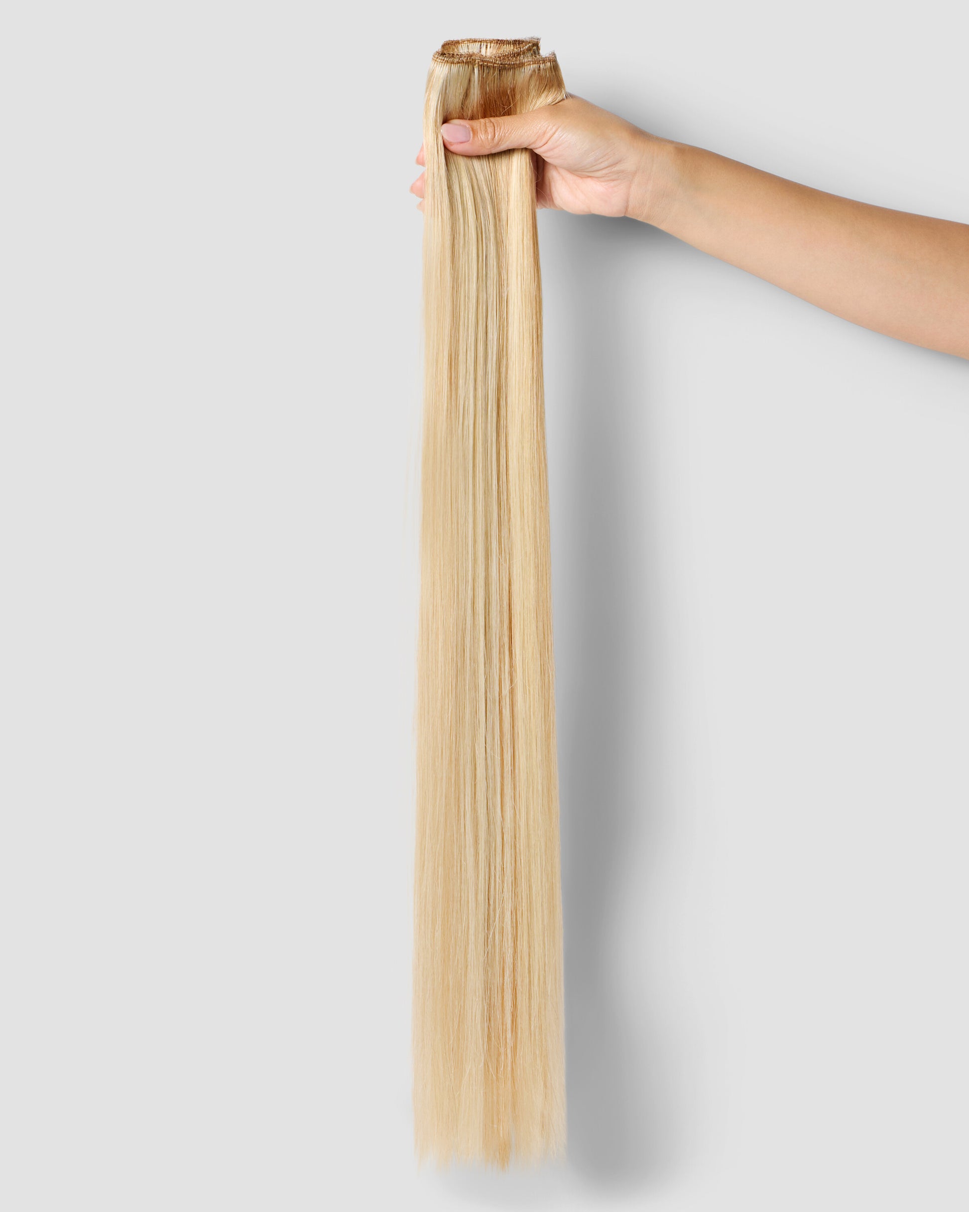 A hand gently holding long blonde hair extensions, showcasing a honey beach hair extension for a stylish look.