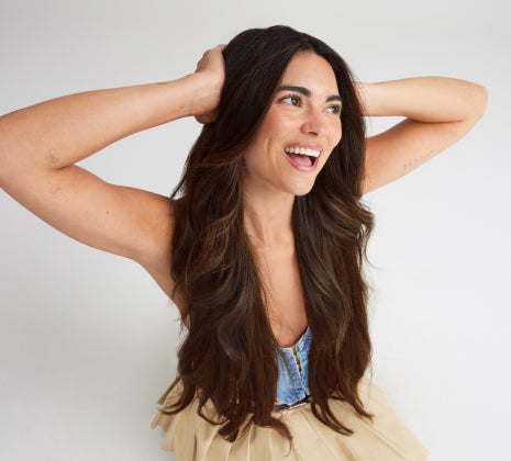 A woman with long hair extensions wearing a blue top placed her hands on her head.