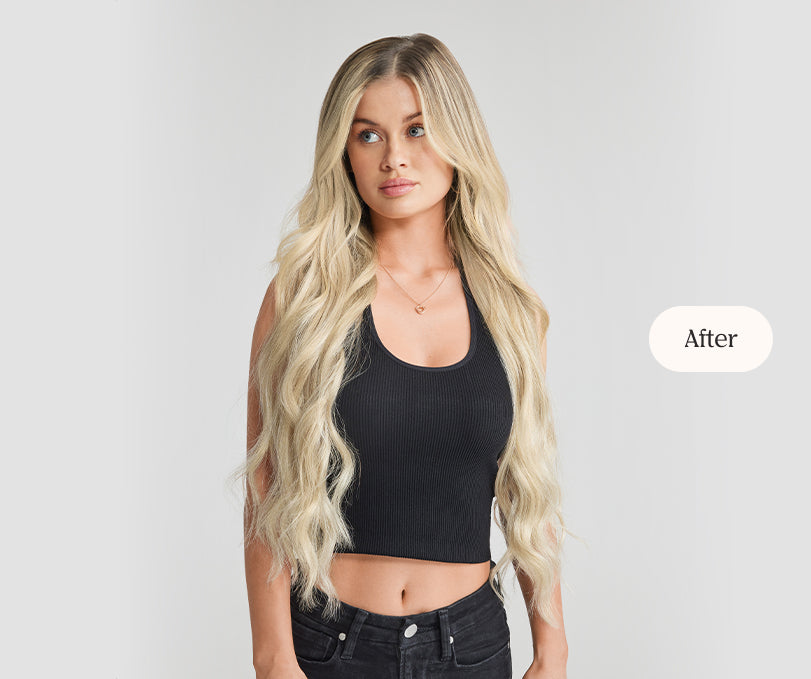A woman dressed in a black crop top and jeans, displaying her hair extension application.