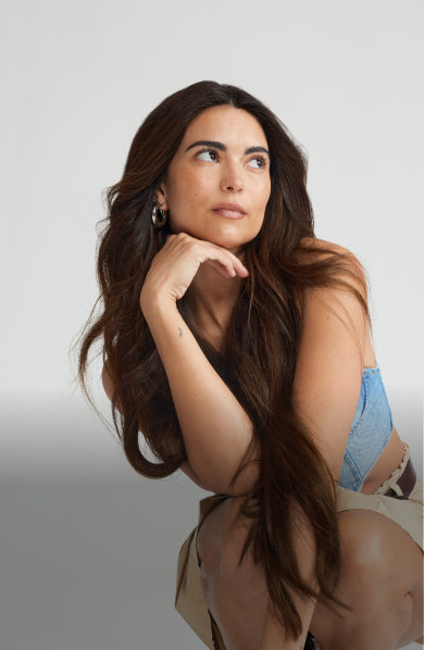 A woman with long hair extensions sits gracefully on a chair, showcasing her stylish look.