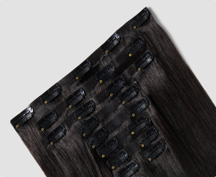 A dark brown clip-in hair extension is displayed on a white background.