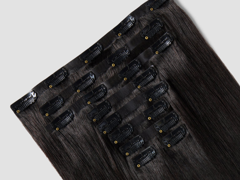 A natural black clip-in hair extension is displayed on a white background.