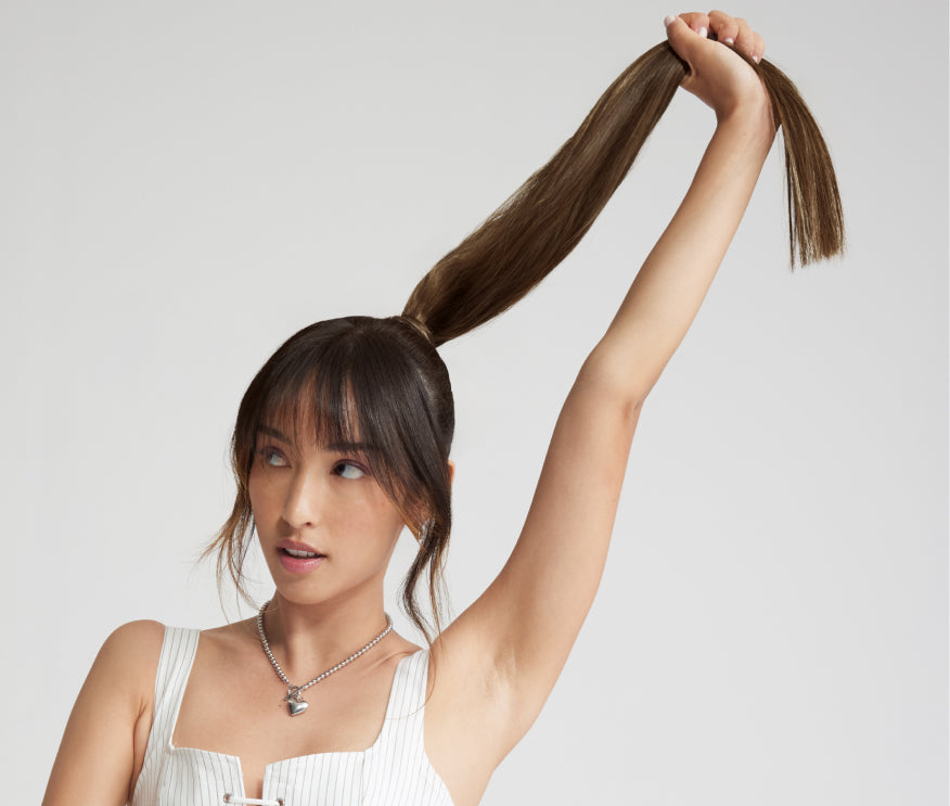 A woman in a ponytail gathers her hair, showcasing her extensions for added length, volume, and style.