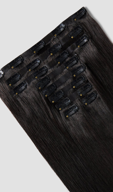 A natural black clip-in hair extension is displayed on a white background.