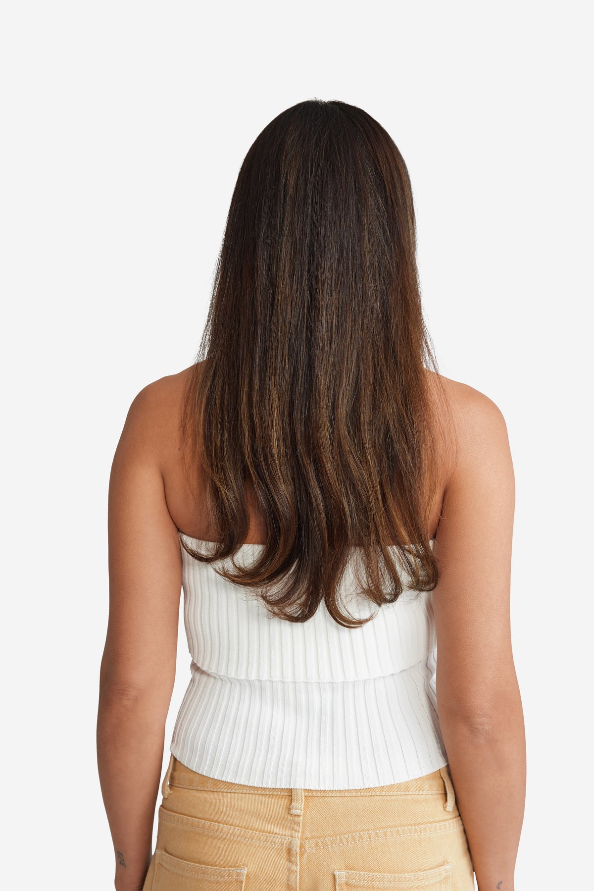 A back view of a woman in a white top and tan pants, showcasing her natural hair.