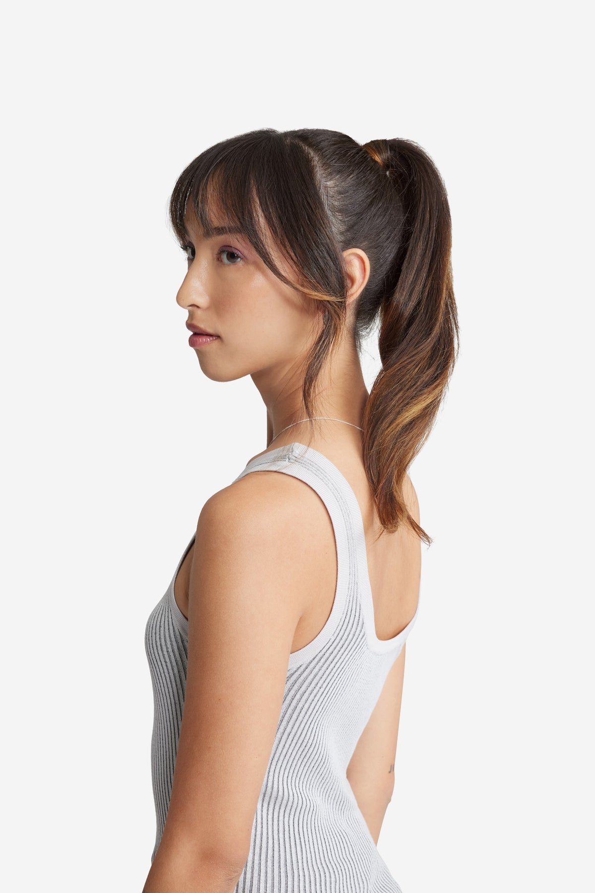 A side view of a woman in a white top with a ponytail, showcasing her natural hair.