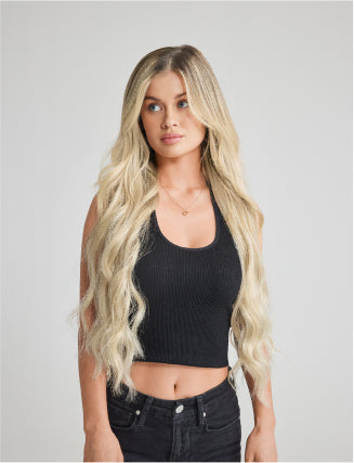 A woman in a black crop top and jeans poses confidently, showcasing long hair extensions.