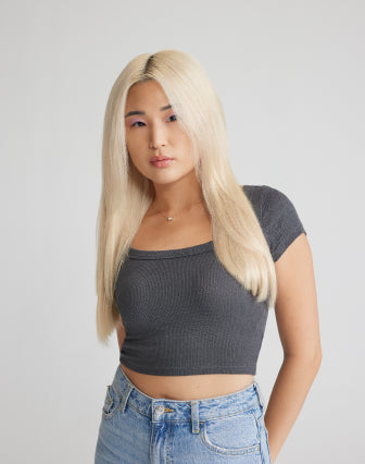 A woman with blonde hair extensions, wearing jeans and a crop top, poses confidently against a neutral background.