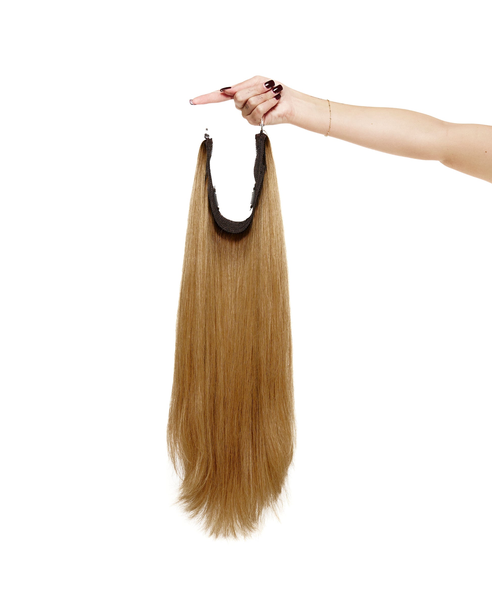 A woman's hand gently holds a long halo hair extension, showcasing its length and texture against a neutral background.