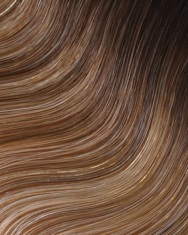 A swatch of wavy hair featuring brown and blonde highlights, enhanced with hair extensions for added volume.