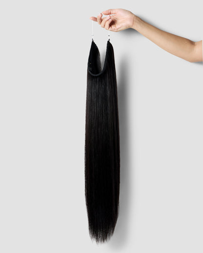 A hand gently holding a long, natural black hair extension, showcasing its smooth texture and rich color.