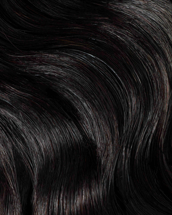 A close-up of natural black hair extensions featuring long, wavy strands, showcasing their texture and shine.