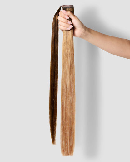 A woman holding a chestnut brown ponytail hair extension in her hand, showcasing its length and texture.