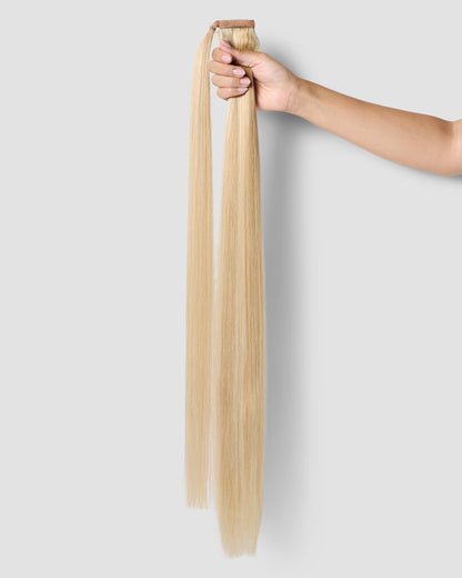 A hand gently holds a long ponytail of Honey Beach Blonde hair extensions, showcasing its vibrant color and length.