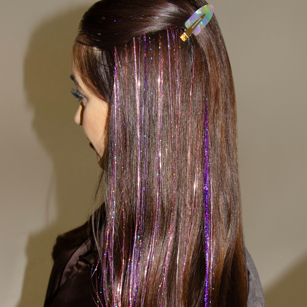 A woman with long brown hair adorned with a purple and green hair clip, featuring tinsel hair extensions for added flair.